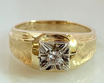 May include: A gold ring with a square-shaped setting featuring a single diamond.