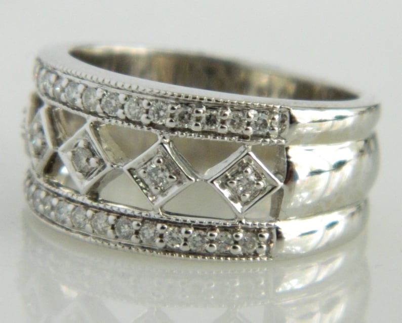 Pu&ograve; includere: Un anello a fascia d'argento con un designo tempestato di diamanti. L'anello presenta un delicato motivo traforato con pi&ugrave; file di piccoli diamanti.