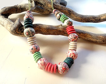 Puede incluir: Un collar colorido hecho de cuentas de cerámica con motivos florales en rojo, verde y blanco. Las cuentas están enhebradas en un cordón verde.