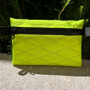 May include: A small, bright yellow zippered pouch with a diamond pattern. The pouch has a black zipper and black straps.
