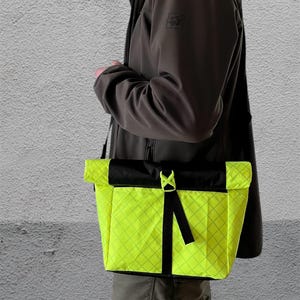 May include: A bright yellow crossbody bag with a black strap and a black flap. The bag has a diamond pattern and a reflective finish.