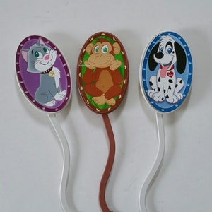 May include: Three whimsical, cartoon-style bookmarks. One features a gray cat with a purple background, another a brown monkey with a green background, and the last a Dalmatian dog with a blue background. Each has a curved stem.