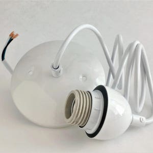 May include: White ceramic ceiling light fixture with a white cord and a white socket. The cord is coiled and the socket is attached to a white ceramic base.