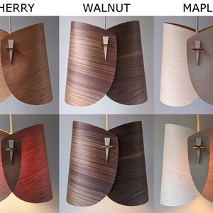 May include: Three pendant lights with wooden shades in cherry, walnut, and maple wood. The shades are made of thin, curved wood and have a cross-shaped detail in the center.