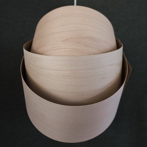 May include: A wooden pendant light fixture with three layers of wood, each with a different grain pattern. The light fixture is hanging from a white cord.