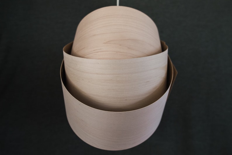 May include: A wooden pendant light fixture with three layers of wood, each with a different grain pattern. The light fixture is hanging from a white cord.