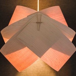 May include: A light wood pendant lamp with a geometric design. The lamp is made of multiple pieces of wood that are joined together to create a unique and modern look.
