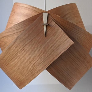 May include: A wooden pendant light fixture with a unique, folded design. The light fixture is made of multiple pieces of wood that are folded and interlocked to create a geometric shape. The light fixture has a warm, natural wood finish.