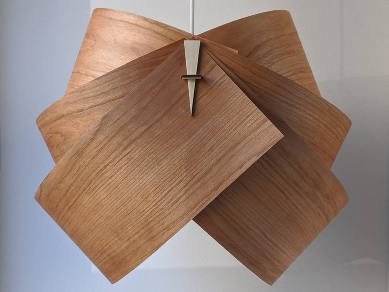 May include: A wooden pendant light fixture with a unique, folded design. The light fixture is made of multiple pieces of wood that are folded and interlocked to create a geometric shape. The light fixture has a warm, natural wood finish.
