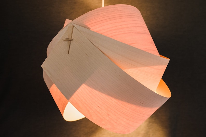 May include: A light wood pendant lamp with a unique, geometric design. The lampshade is made of thin, curved pieces of wood that are joined together to create a swirling, organic shape. The lampshade is illuminated from within, casting a warm glow.