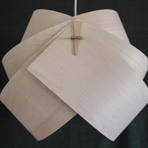 May include: A light wood pendant lamp with a unique folded design. The lamp is held together with a small wooden dowel.