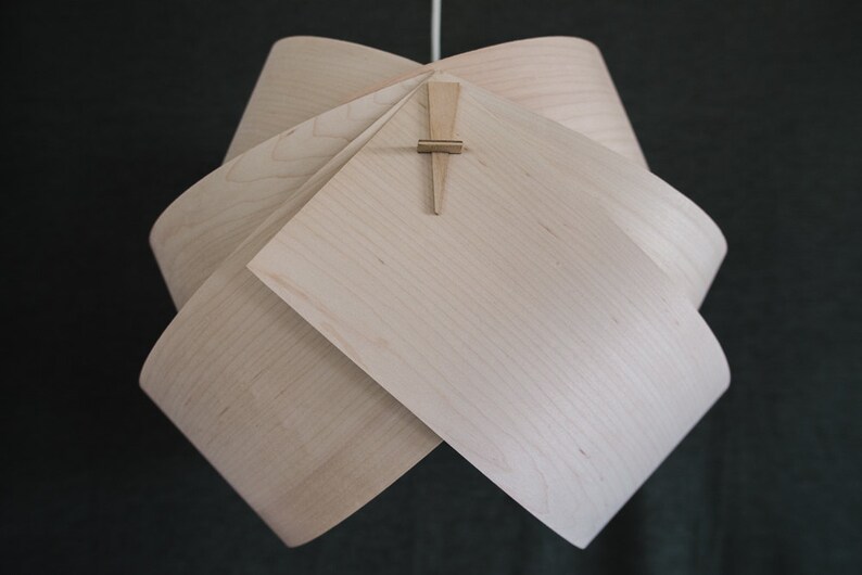 May include: A light wood pendant lamp with a unique folded design. The lamp is held together with a small wooden dowel.