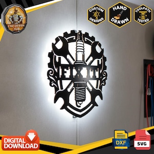 May include: A black wall-mounted sign featuring a central spark plug flanked by two crossed wrenches, all enclosed within a gear-shaped frame. The word FIX IT is displayed horizontally across the center. The sign is backlit with a bright white glow.