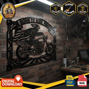 Könnte beinhalten: Ein schwarzes Wandkunstobjekt aus Metall mit der Silhouette eines Motorradfahrers, der einen Helm und einen Umhang mit Sternen und Streifen trägt. Das Design enthält den Text BORN TO RIDE FREE in einem Banner über dem Fahrer.