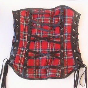 May include: A red and black plaid corset with black ribbon lacing and grommets. The corset has a black leather trim.