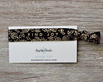 May include: Black hair tie with a gold floral pattern and the text "FIND JOY". The hair tie is on a white card with the text "Azurea Studio" and "HAIR TIE" in blue text.