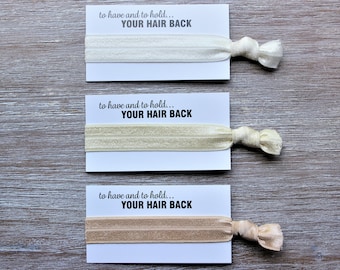 May include: Three hair ties in cream, beige, and tan, each on a white card. The cards read "to have and to hold... YOUR HAIR BACK" in black text. The background is a light wood grain pattern.