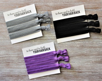 May include: Three sets of hair ties on white cards with the text "to have and to hold... YOUR HAIR BACK". The hair ties are in silver, black, and purple.