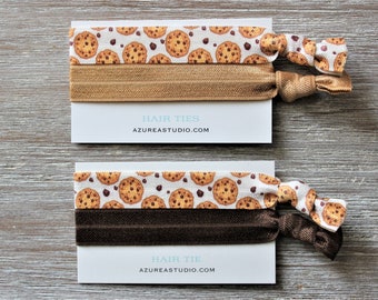 May include: Two sets of hair ties featuring a chocolate chip cookie design. The top set includes two brown hair ties, while the bottom set has one brown hair tie. The card displays the text "Hair Ties" and "Azureastudio.com".