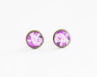 May include: A pair of small, round stud earrings with a purple and white floral design.