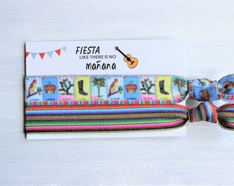 May include: Two colourful hair ties with a striped pattern and a pattern of Loteria cards. The hair ties are on a white card with the text "Fiesta like there is no mañana".