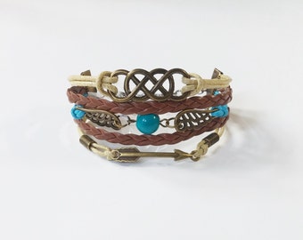 May include: A multi-layered bracelet with brown and cream leather straps, a turquoise bead, and metal accents including an infinity symbol, arrow, and leaves.