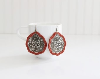 May include: A pair of earrings with a red crocheted border and a silver filigree design.