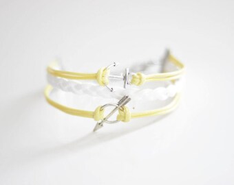 May include: Two yellow braided bracelets with silver charms. One charm is an anchor and the other is an arrow.