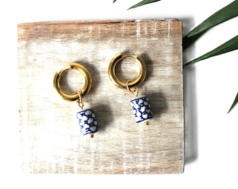 May include: Gold hoop earrings with a blue and white porcelain charm. The charm has a floral pattern.