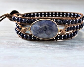 May include: A triple wrap bracelet with a blue gemstone pendant and dark blue beads. The bracelet is made of brown leather and has a tie closure.