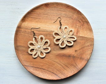 May include: A pair of crocheted flower earrings with a pearl bead in the center. The earrings are beige and have a bronze hook.