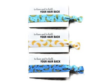 May include: Three hair ties with a blue and white banana print and a yellow and white banana print. Each hair tie is attached to a card that reads "to have and to hold... YOUR HAIR BACK".
