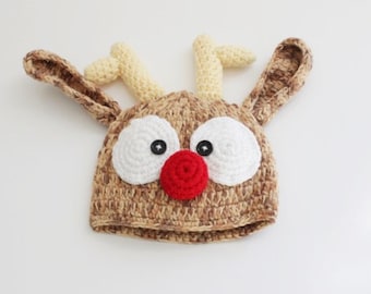 May include: A brown knitted reindeer hat with white yarn eyes, a red yarn nose, and yellow yarn antlers.