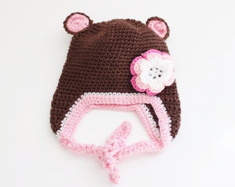 May include: Brown crocheted hat with pink and white flower detail and a pink tie.