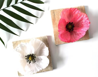 May include: Two wooden coasters with a single poppy flower on each. One coaster has a pink poppy and the other has a white poppy.