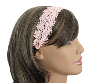 May include: A pale pink lace headband with a decorative, wavy pattern. The headband is worn by a person with brown hair and a fair complexion. A delicate, feminine hair accessory.