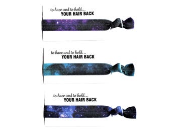 May include: Three elastic hair ties with galaxy prints in purple, blue, and dark blue, each knotted and attached to a white card featuring the black printed text: to have and to hold... YOUR HAIR BACK. The hair ties are arranged vertically.