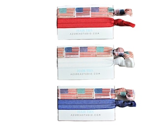 May include: Three sets of hair ties with American flag designs. Each set includes a white elastic hair tie and a patterned hair tie in red, white, and blue.