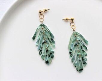 May include: A pair of green leaf-shaped earrings with gold accents. The earrings are made of a layered, marbled material.
