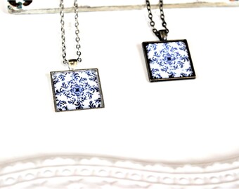 May include: Two silver and black necklaces with square pendants featuring a blue and white patterned design.
