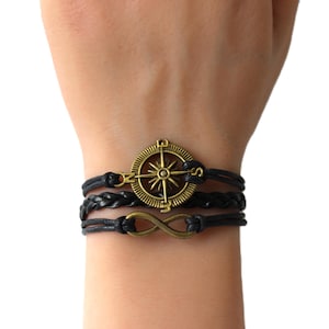 May include: A black leather bracelet with a compass charm and an infinity symbol charm.
