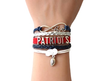 May include: A stack of bracelets in a red, white and blue colour scheme. The bracelets feature a silver infinity symbol with the word "love" inscribed, a red band with the word "PATRIOTS" in silver letters, and a silver football charm.