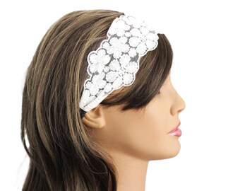 May include: White lace headband with a floral design. The headband is wide and stretches across the forehead. The lace is detailed with a repeating flower pattern. The model has brown hair.