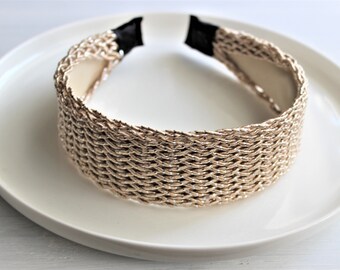 May include: A gold braided headband with a woven design. The headband is on a white plate.