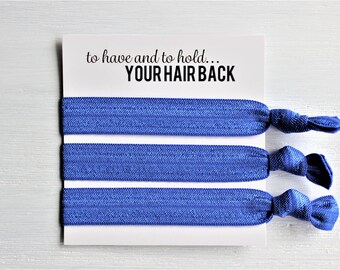 May include: Three royal blue hair ties are displayed on a white card. The card has the text "to have and to hold... YOUR HAIR BACK" in black. The hair ties are knotted at the ends.