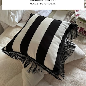 May include: Black and white striped cotton cushion cover with long black fringe trim. "BLACK WHITE STRIPE COTTON, WITH LONG BLACK FRINGE TRIM, CUSHION COVER. MADE TO ORDER."
