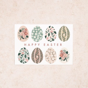 Puede incluir: Una tarjeta blanca con un dise&ntilde;o floral. La tarjeta presenta ocho huevos de color pastel con patrones florales. El texto "HAPPY EASTER" est&aacute; impreso en rosa en la tarjeta.