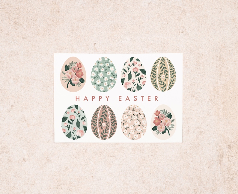 Puede incluir: Una tarjeta blanca con un dise&ntilde;o floral. La tarjeta presenta ocho huevos de color pastel con patrones florales. El texto "HAPPY EASTER" est&aacute; impreso en rosa en la tarjeta.