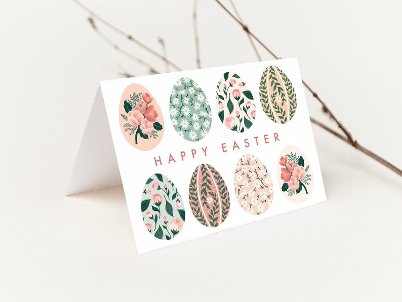 Puede incluir: Una tarjeta blanca con un dise&ntilde;o floral. La tarjeta tiene un patr&oacute;n floral rosa, verde y blanco en los huevos. El texto "Happy Easter" est&aacute; impreso en rosa en la tarjeta.