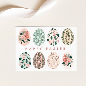 Puede incluir: Una tarjeta blanca con un dise&ntilde;o floral. La tarjeta presenta ocho huevos de color pastel con patrones florales. El texto "HAPPY EASTER" est&aacute; impreso en rojo en la tarjeta.
